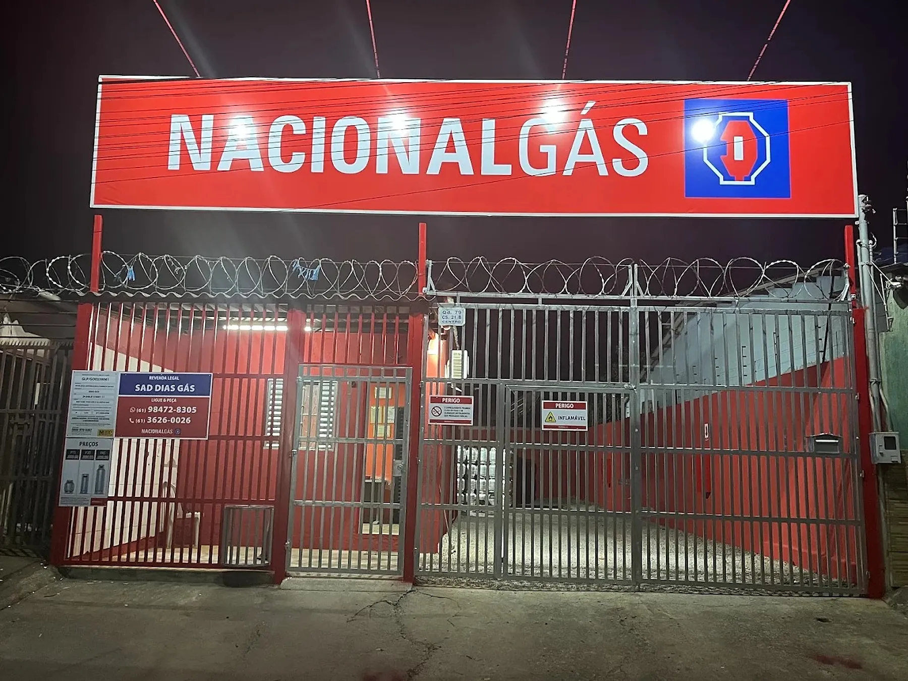 Fachada da Sad Dias Gás à noite, com o letreiro vermelho da Nacional Gás aceso e a placa Revenda legal